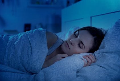 Frau in mit Blackout-Vorhängen abgedunkeltem Schlafzimmer